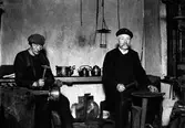 Kopparslagare Johan Gustafsson (till höger) i sin kopparverkstad tillsammans med Frans Fröman (till vänster). Båda med hammare i höger handen.
Verkstaden var möjligen belägen i ett gårdshus i kv Hjorten 3.