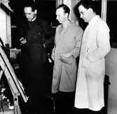 Tre män står och tittar på en ritning. AB Elektro-Apparat i kvarteret Yxan.

Från vänster:
Gösta Odeus, förman.
B Mellblom, ingenjör.
G Holmér, ingenjör.