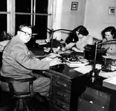 Kassakontoret på AB Elektro-Apparat i kvarteret Yxan.

Från vänster:
Agne Linde, kontorschef.
Aina Johansson, kontorsbiträde.
Gittan Brovall, kontorsbiträde.