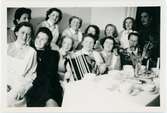 Gruppbild. Sjukvårdsklädda kvinnor vid bord dukat med kaffekoppar