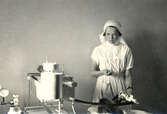 Bilden visar en sjuksköterska som utför ämnesomsättningsundersökning på en patient. Tiden kan vara 1930-40 tal.
