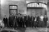 Ett femtontal män ur Alingsås Verkstäders personalstyrka.

Från vänster:
xxxx.
xxxx.
xxxx.
xxxx.
xxxx.
xxxx.
xxxx.
Alfred Lans.
xxxx.
Eliasson.
xxxx.
xxxx.
Frisk.
xxxx.
Artur Eriksson.