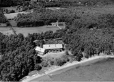 Flygbild över Konvalescenthemmet Meryt, Vickan Onsala. Meryt invigdes 1901 och uppfördes på initiativ av Blanche Dickson på Tjolöholm. Då var omgivningen helt kal, men här kryper skogen nära inpå byggnaden, som ligger nära stranden i Kungsbackafjorden med brygga och eka. I bakgrunden ses en liten gård med åkrar.