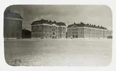 Vy över ett nybyggt (?) regemente en vintrig dag, 1914. 
Några meniga är på väg över kaserngården.'
Jfr HYCA1090.