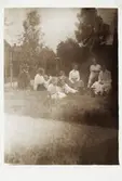 En familj sitter på gräsmattan i en trädgård. 1910-tal.