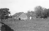 Gårdsbebyggelse och hagar på Knastås i Onsala. Boningshusets ena fönster har stängda fönsterluckor och dörren är försedd med ett smalt överljus, vanligt i trakten.