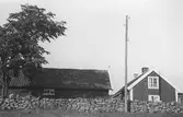 Lantgård vid Häcklahagsvägen, Onsala. Bostadshus och ekomomibyggnad bakom en stenmur. Framför gärdsgården står en elstolpe.
