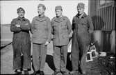 Fyra beredskapsmän står invid en husknut; två bär uniform, två har overall. Bakom dem skymtar ett par svagdrickabackar med tomma flaskor.