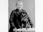 Porträtt av en pojke och en hund. Båda har rosett om halsen. Beställare: Jenny Andersson, Almeberg, Varberg, troligen pojkens mor.