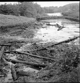Bearbetade stockar som framkommit vid arkeologiska utgrävningar av den inre vallgraven vid Rumlaborg i Huskvarna sommaren 1935. I bakgrunden syns pumpen som användes för att hålla vatten undan från vallgraven och i fjärran syns den gamla bron över Huskvarnaån.