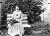 Kvinna sitter på en bänk med kvistar i handen, Uppland