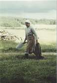 Hilda Sandberg (1887-1973) går på en grusväg bärandes på en skyffel och en säck, 