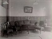 Utställning. Interiör från Öbergs möbelaffärs utställningsmonter på Hantverksmässan 1927 i Gamlebyskolan, Varberg. Montern är inredd som ett vardagsrum med en soffgrupp.