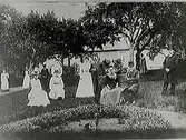 Herrskap och tjänstefolk samlade i en trädgård framför en byggnad i Slöinge.