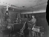 Apoteket Kronans vattenfabrik, Varberg. Alfred Petersson och John Nilsson står vid apparaterna i källaren.
(Fotografiet är skadat i högerkanten)