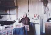 Hilda Sandberg (1887-1973, född Olsson) sitter i sitt kök och dricker kaffe, 