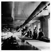 Interiörsbild från Silfas textiltryck. Vid de långa tryckborden står 9 män i förkläde.