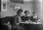 Tre kvinnor sitter i en soffa och tittar i en skrift