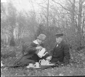John Algot Carlsson på utflykt i en skogsdunge med kvinnligt sällskap i vårhatt. De har dukat upp med porslinsservisen och hon häller upp åt honom ur kaffekannan. Omkring 1915.