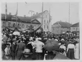 En folksamling på Stora Torget i Alingsås. Amerikanska flaggan syns och troligen pågår firandet i samband med Svenska Chicago-körens turné genom Sverige 1920.