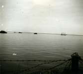 10 maj 1945. Vy över Kalmarsund. En landstigningsbåt syns i fjärran. Ombord är balter i tysk uniform och tyska soldater. De kom från det sista tyska brohuvudet i Kurland. Ungefär 3000 soldater flydde.  Ungefär hälften kom till Kalmar. Här internerades de i läger på Kullö innan de fördes över till Eksjö. En del av dem utlämnades sedan, i enlighet med stilleståndsavtalet, till Sovjet.