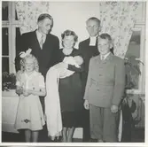 Dop av ett litet barn där familjen och prästen står samlade i ett rum, okänd plats och årtal. Foto från Sagered-album.