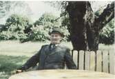 Robert Sandberg (1880-1961) sitter och vilar på en bänk i trädgården, 