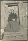 Anna Brita Svensdotter, född 1842 i Fotskäl, sitter framför en trädörr i Hajom (Mark), okänt årtal. Hon var mor till Adolf Johansson (1868-1935), Labacka 1:2 