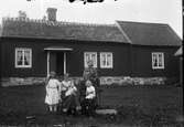 Sällstorp, Klingeberg, Hästhagen (Danskens). Linnea och Klas med sina fyra barn samlade på gården framför bostadshuset med halmtak. Till höger finns en tillbyggd del som är någon högre och har enkupigt tegeltak. Till höger skymtar en ekonomibyggnad, även den med halmtak.