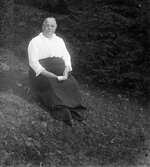 Constance Engström sitter i en gräsbacke med en anteckningsbok i knät. Hon var moster till fotografen och folkskollärare i Sällstorp åren 1891-1921. Gunnar Engström tog över hennes tjänst och arbetade som lärare till pensionen 1960.