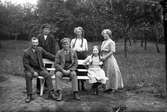 Familjen Hansson, Syllinge, Hansa i Veddige. Till vänster Julius Hanssson och till höger systern Gärda. Familjen är samlad kring en soffa i trädgården. Döttrarna bär flätor.
(Se även bild nr GEB172)
