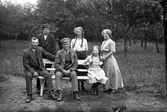 Familjen Hansson, Syllinge, Hansa i Veddige. Till vänster Julius Hanssson och till höger systern Gärda. Familjen är samlad kring en soffa i trädgården. Döttrarna bär flätor.
(Se även bild nr GEB172)