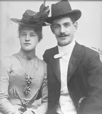 Parporträtt av Ellen Persson född Almskog 15/8 1879 - 3/3 1963 och Per Axel Oskar Persson 9/1 1873 - 18/4 1948. 
Både mannen och kvinnan bär hattar. Kvinnan har en brosch vid kragen. Föräldrar till givaren Sven Persson.