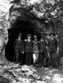 Fem välklädda herrar framför en gruvingång.
























