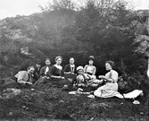 Sällstorpsbor i olika åldrar på picnic i naturen, uppe på ett berg vid några granar. Från vänster: nr 3 Anna-Britta Börjesson (Johans); nr 4 Anna-Emelia Börjesson (syster till Ragnar B.); nr 5 Bertha Engström (fotografens mor); nr 6 Ragnar Börjesson; nr 8 Alma Andersson (f. Börjesson).

Kopparpannan med kaffe står i gräset framför Anna-Emelia i prickig klänning, liksom mjölkflaskan och kakfatet. Man dricker ur mönstrade porslinskoppar. Lille Ragnar håller i en kikare.