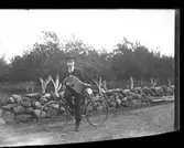 Sällstorp 6. Ynglingen Nils från Jannes med cykel och ett enradigt durspel (dragspel) framför Ahlbergs trädgård, 1915 eller strax före. Fruktträdens stammar är vitkalkade för att inte bli så varma på senvintern, och därmed få barkskador. Kalk hjälper också till att skydda mot äggläggande skadedjur i barken.