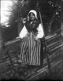 Flicka i folkdräkt sitter på gärdesgård, Dalarna