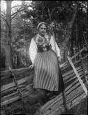 Kvinna i folkdräkt sitter på gärdesgård, Dalarna