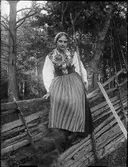 Kvinna i folkdräkt sitter på gärdesgård, Dalarna