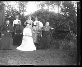 Systrarna Engström tillsammans med en grupp äldre kvinnor i en trädgård. Constance sitter med mönstrad klänning näst längst till höger med Bertha stående bakom och Fredrika sittande framför.