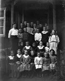 Elever samlade med lärarinnan på skolans farstukvist. Pojkarna står upptill och flickorna, utom en, sitter ned framtill.