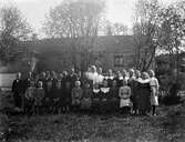 Folkskollärarinnan Constance Engström tillsammans med sina elever utanför skolan i Sällstorp en solig dag. Pojkarna står till vänster och flickorna till höger i bild. (Negativet skadat till vänster)