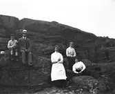 Sju personer sitter på ett kalt berg. En pojke och en man i hatt sitter och dinglar med benen på en liten avsats.