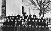 Konfirmandklass vid Tvååkers kyrka. Prästen bär kubb och alla är svartklädda. Ada Selvén sitter på främsta raden som nummer fem från höger.