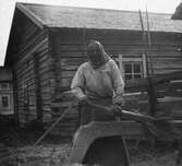 En äldre kvinna som står och bereder lin med en linbråka. Resele cirka 1925.