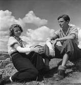 Ungdomar, pojke och flicka sitter och vilar på en kulle. Båda med bandage på ena armen.