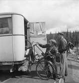 Lastning av cykel i bagagerummet på en postbuss. Två män med kepsar och ryggsäckar lyfter in en cykel i bussen.