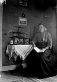 Småskollärarinnan Bertha Engström sitter i hemmet vid ett bord med fotografier på hennes mor Anna och far Carl, samt två präster.