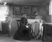 Fredrika Engström, moster till fotografen, sitter i finrummet med stora fotografier på väggen av hennes far Carl och mor Anna.