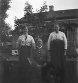 Tre kvinnor vid en rosenbuske framför bostadshuset. Troligen är de ur tre generationer i familjen. (Se interiörbild nr GEB233)